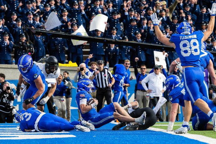 Air Force quarterback Liam Szarka sits in the end zone after scoring a fourth-quarter touchdown against Army as teammates and cadets celebrate.