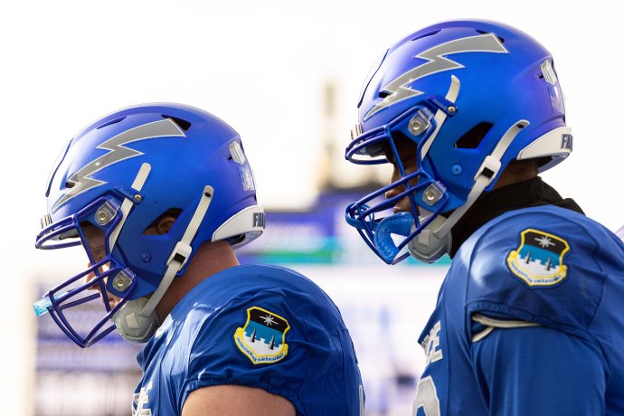 Two Air Force football players stand in helmets and blue uniforms during pregame at Falcon Stadium.
