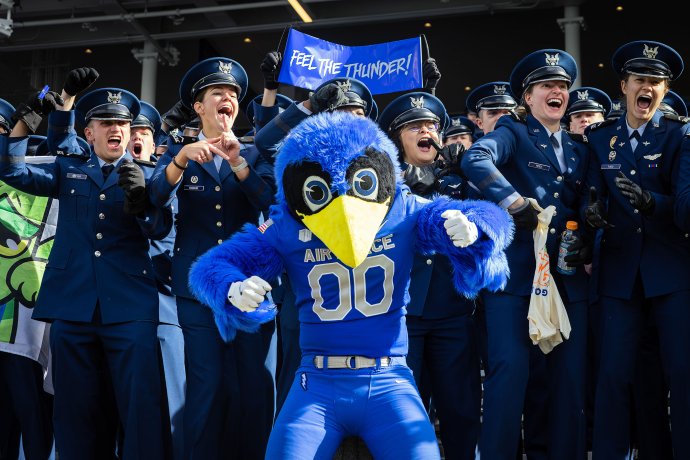 The Air Force Falcons bird mascot poses in front of cheering U.S. Air Force Academy cadets, including one holding a “Feel the Thunder!” sign.