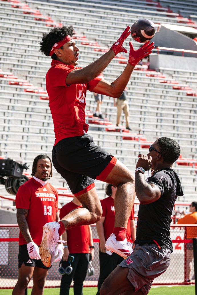 A Nebraska receiver leaps and reaches for a football during pregame warmups at Memorial Stadium.