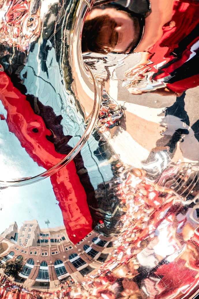Memorial Stadium and the surrounding game-day scene are reflected in the bell of a tuba.
