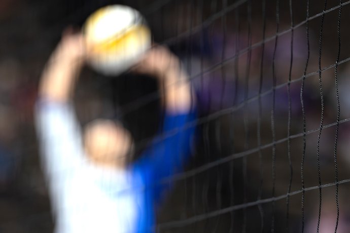 A blurred Dallas setter warms up behind a sharply focused volleyball net.