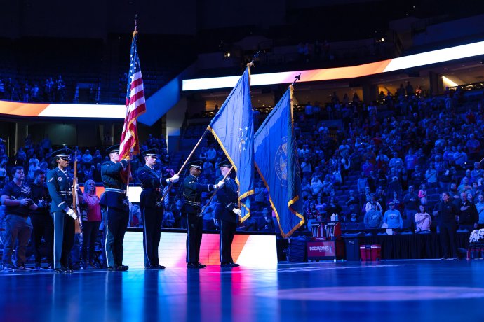 Members of the Offutt AFB Honor Guard present the colors on the court before the game as spectators stand in the arena.